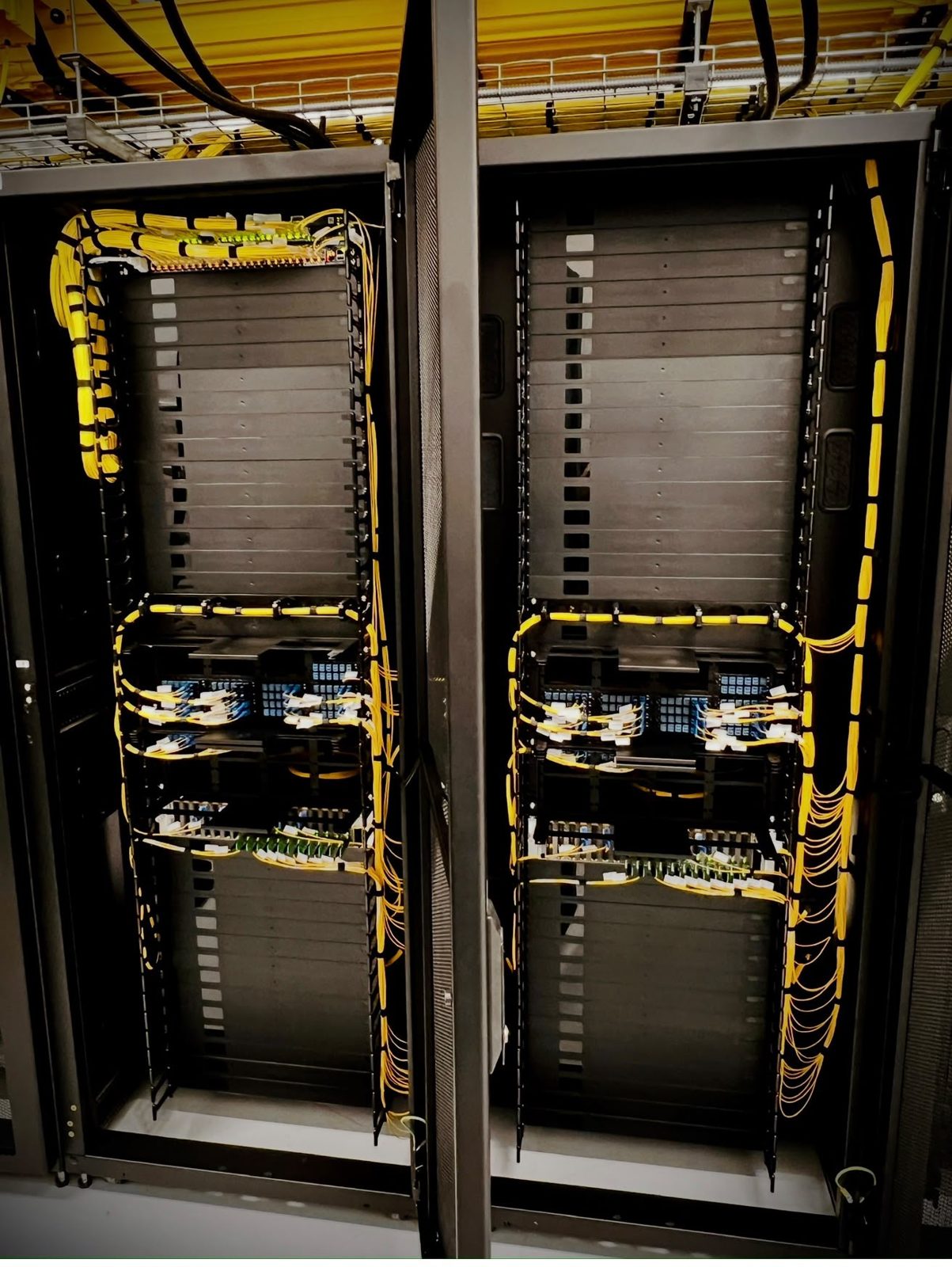 Two open cabinets with yellow fibre looms and patch panels