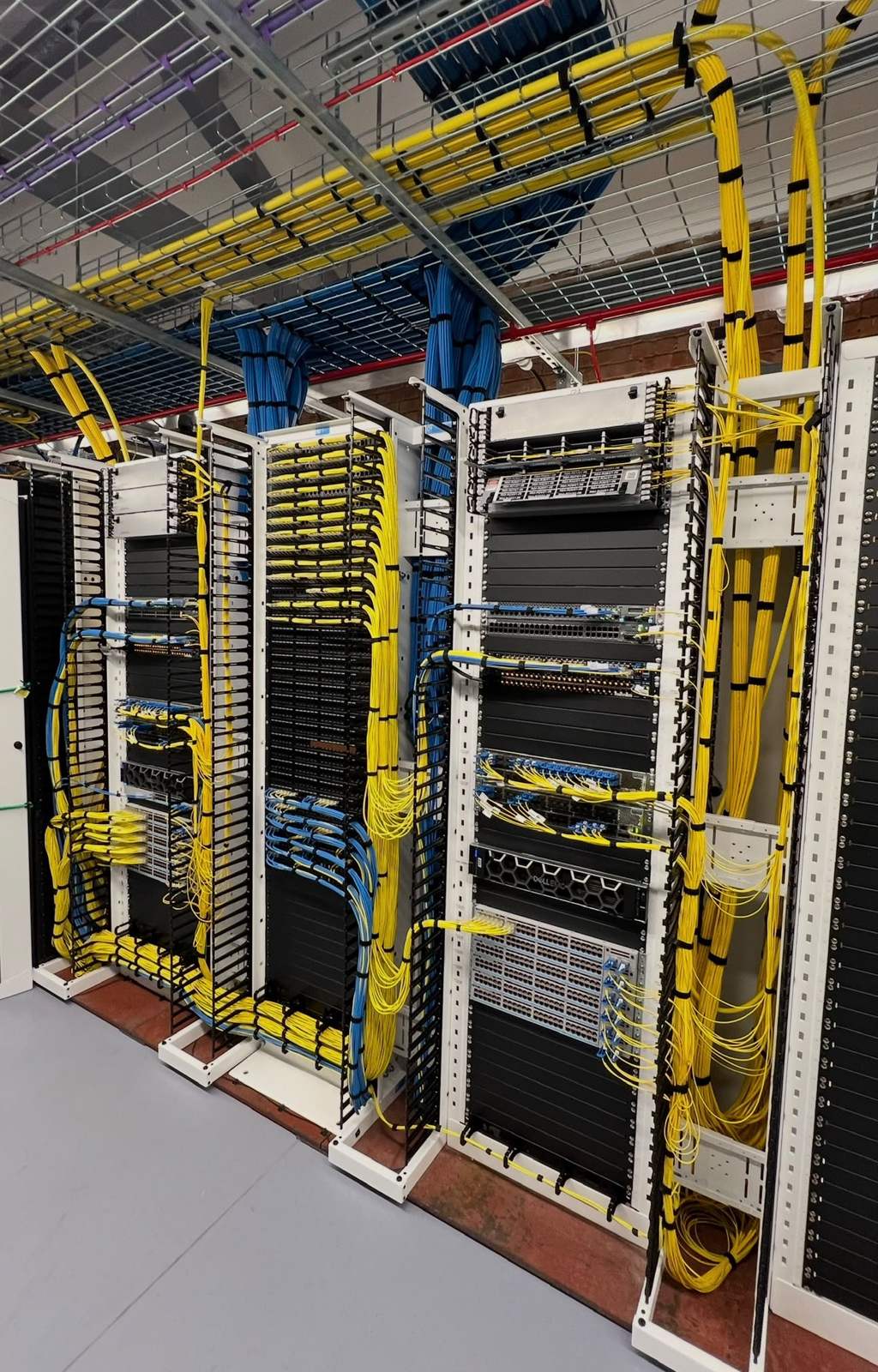 Row of data centre racks with overhead yellow fibre trays